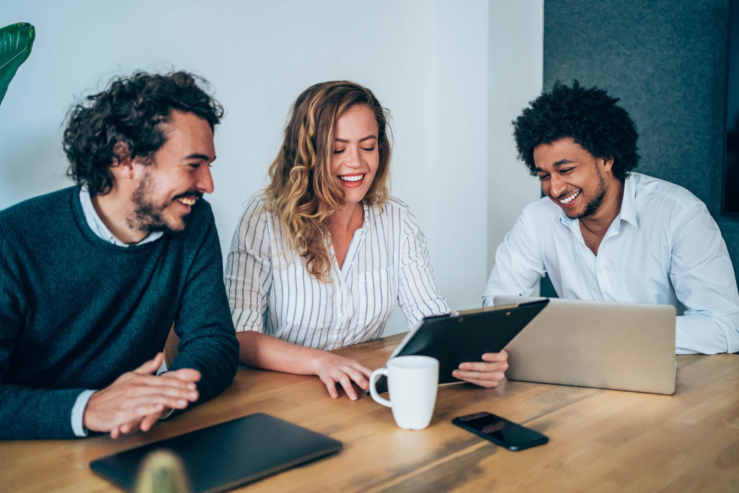 Three business people looking at a screen while working together at a desk.