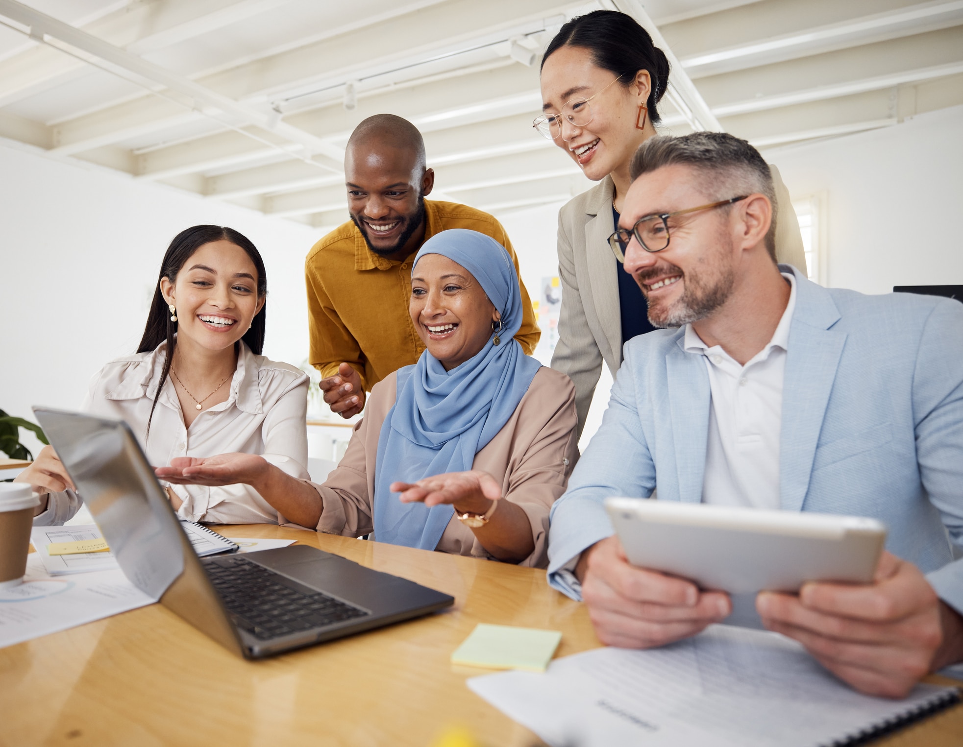 A group of business people discussing work in front of a laptop in an office. The mood is lively and friendly. 