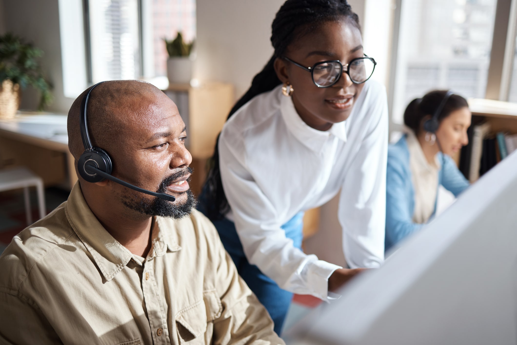 People in an office or call center wearing headsets and looking at a computer together