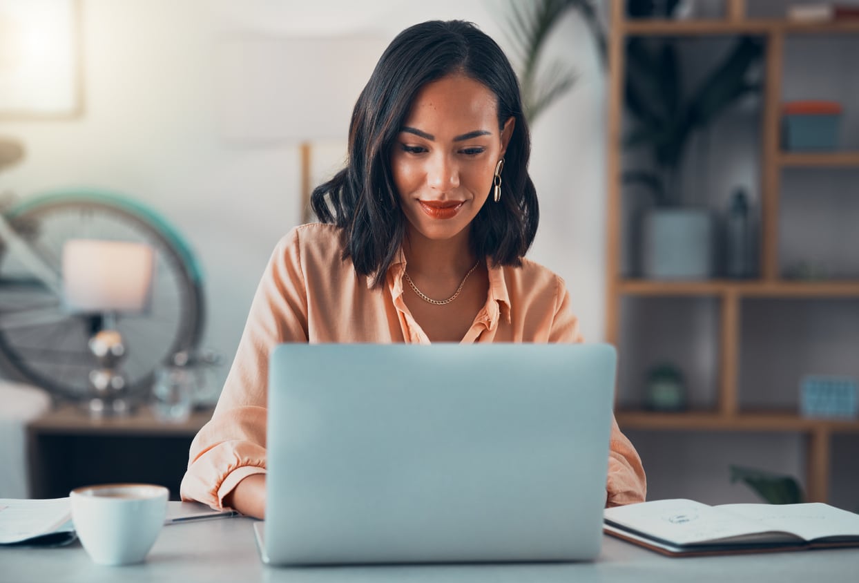 Smiling woman working on laptop sitting alone at office desk