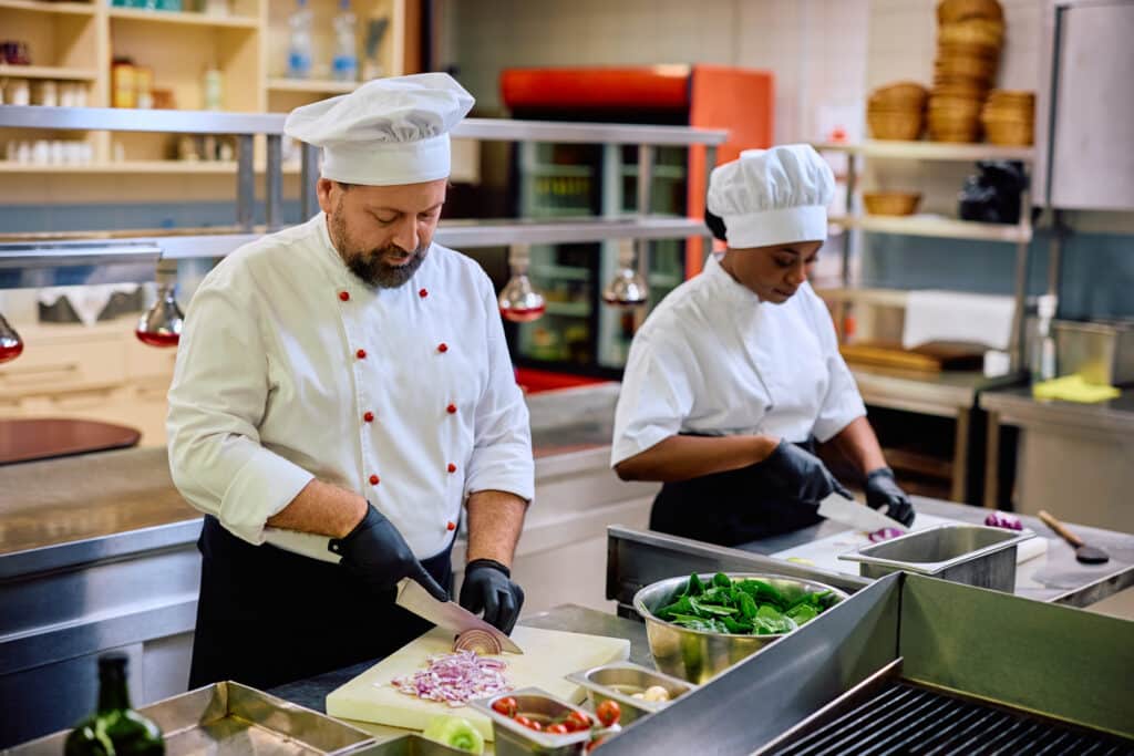 Two professional cooks preparing food while working in the kitchen in a restaurant. Focus is on male chef.