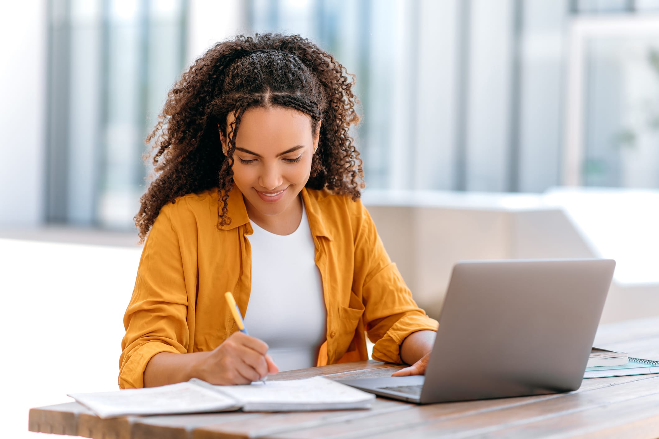 Person writing in a notebook next to an open laptop