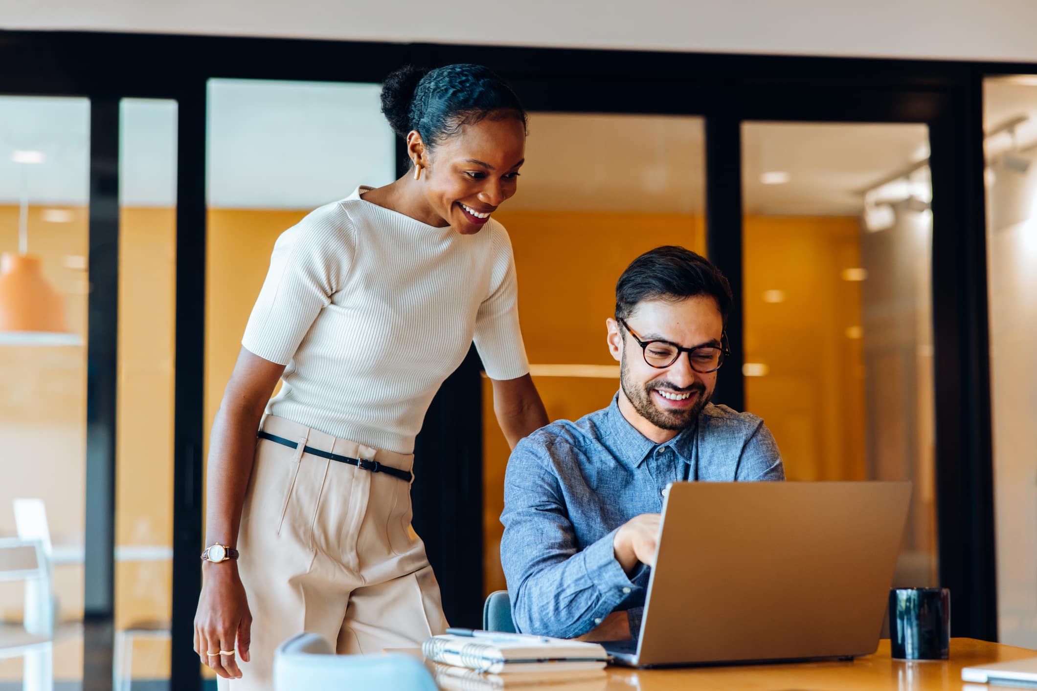 Coworkers smiling and working together on a laptop in a professional office setting