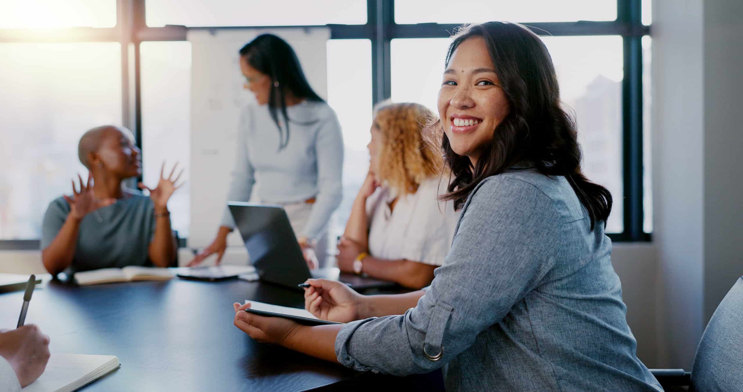 Woman smiling at the camera while sitting at a conference table with other professional women