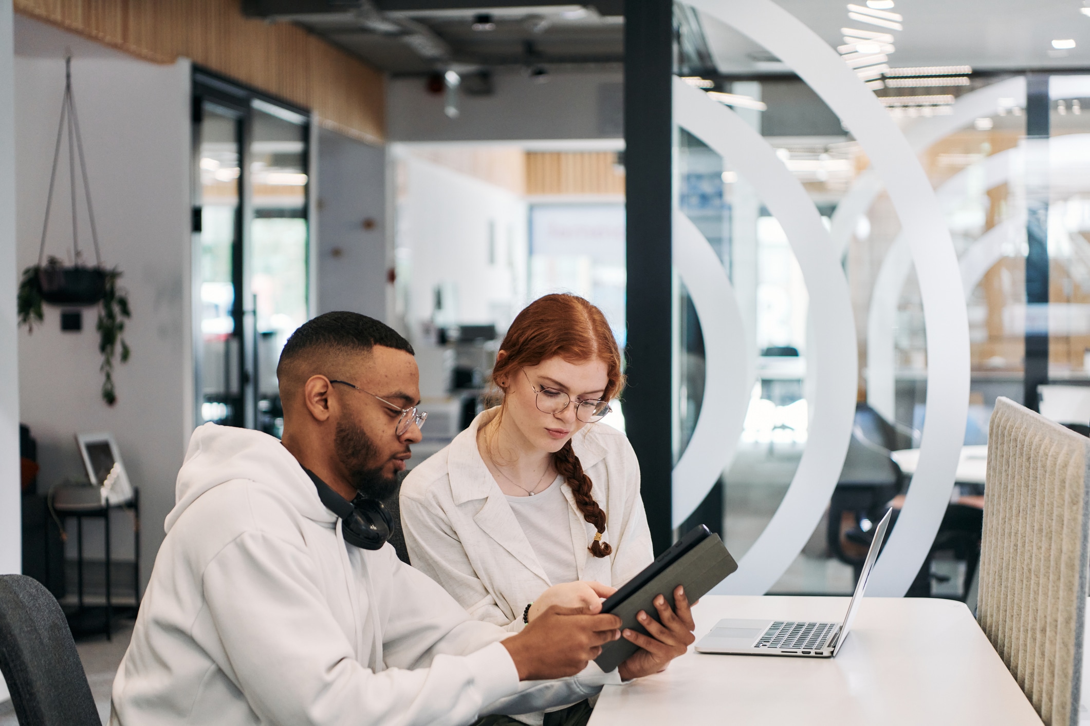 Two colleagues collaborating in a modern office while discussing a project using a tablet and laptop
