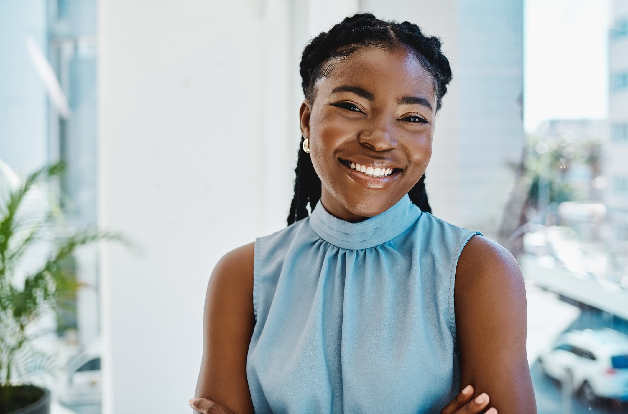 Confident young Black businesswoman standing at a window and smiling in an open, well-lit office.