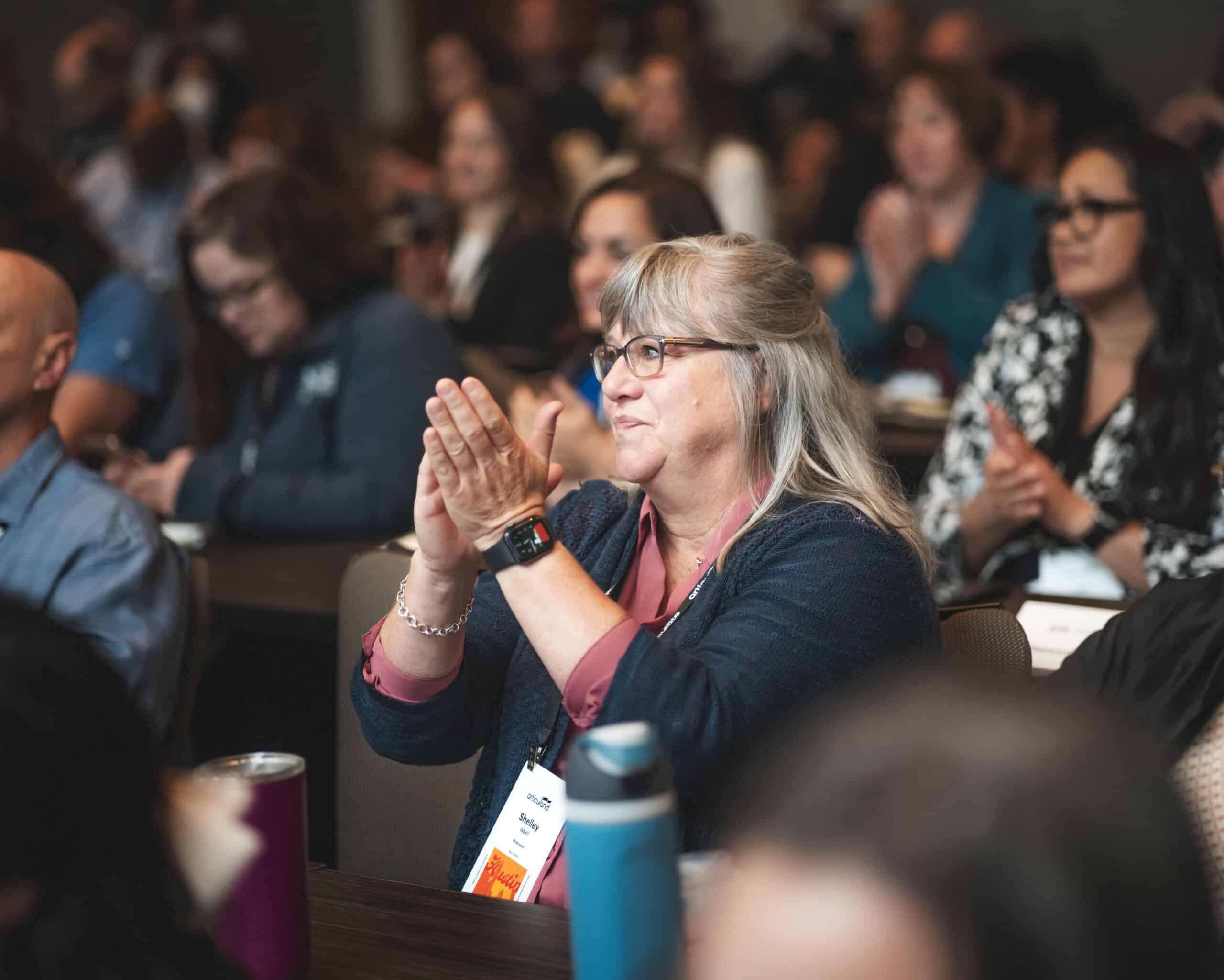 Audience member clapping and sitting in a crowd of people