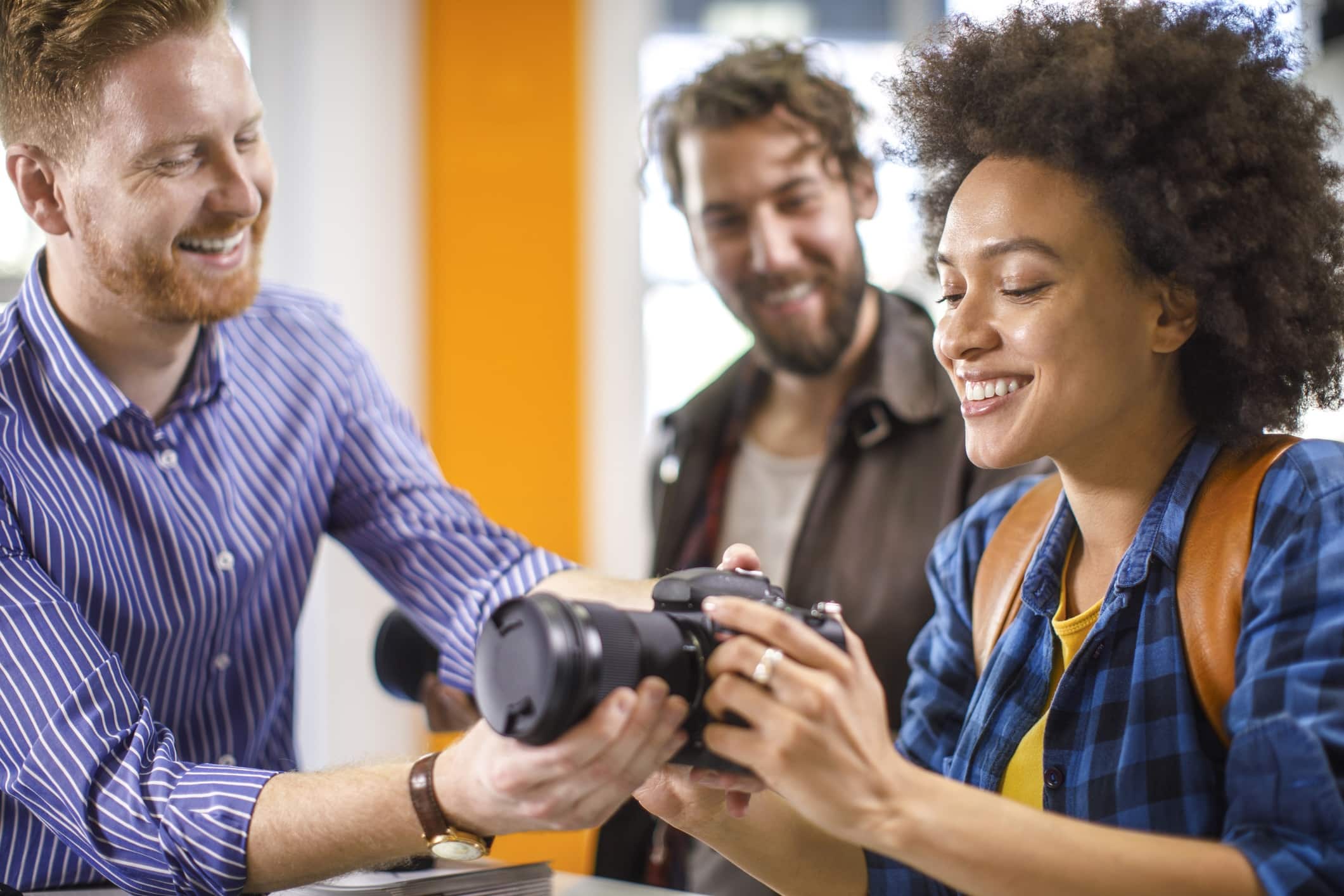 A smiling customer holds a camera and talks with a salesperson in a camera store.