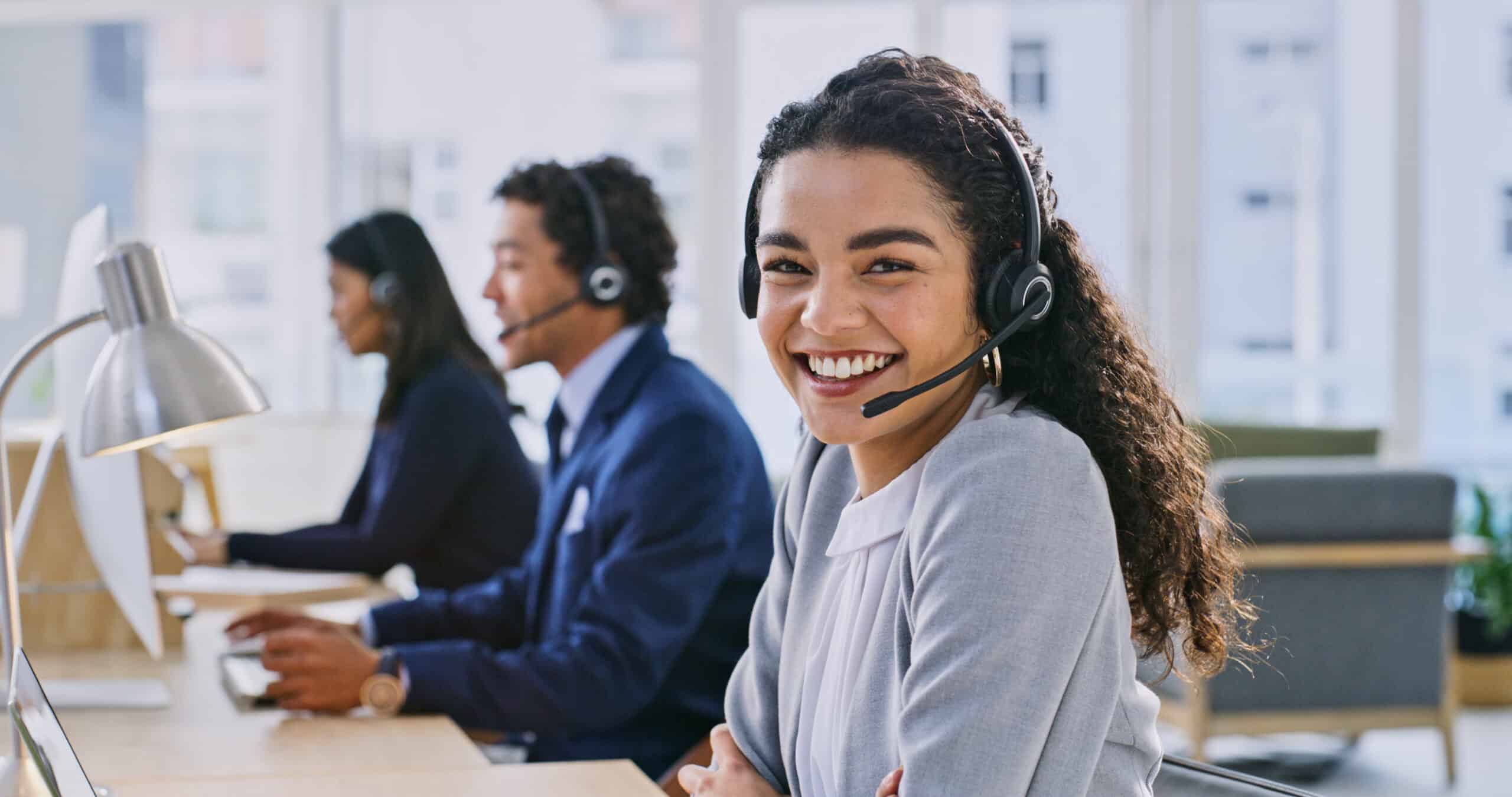 Customer service representative smiling while wearing a headset in a call center.