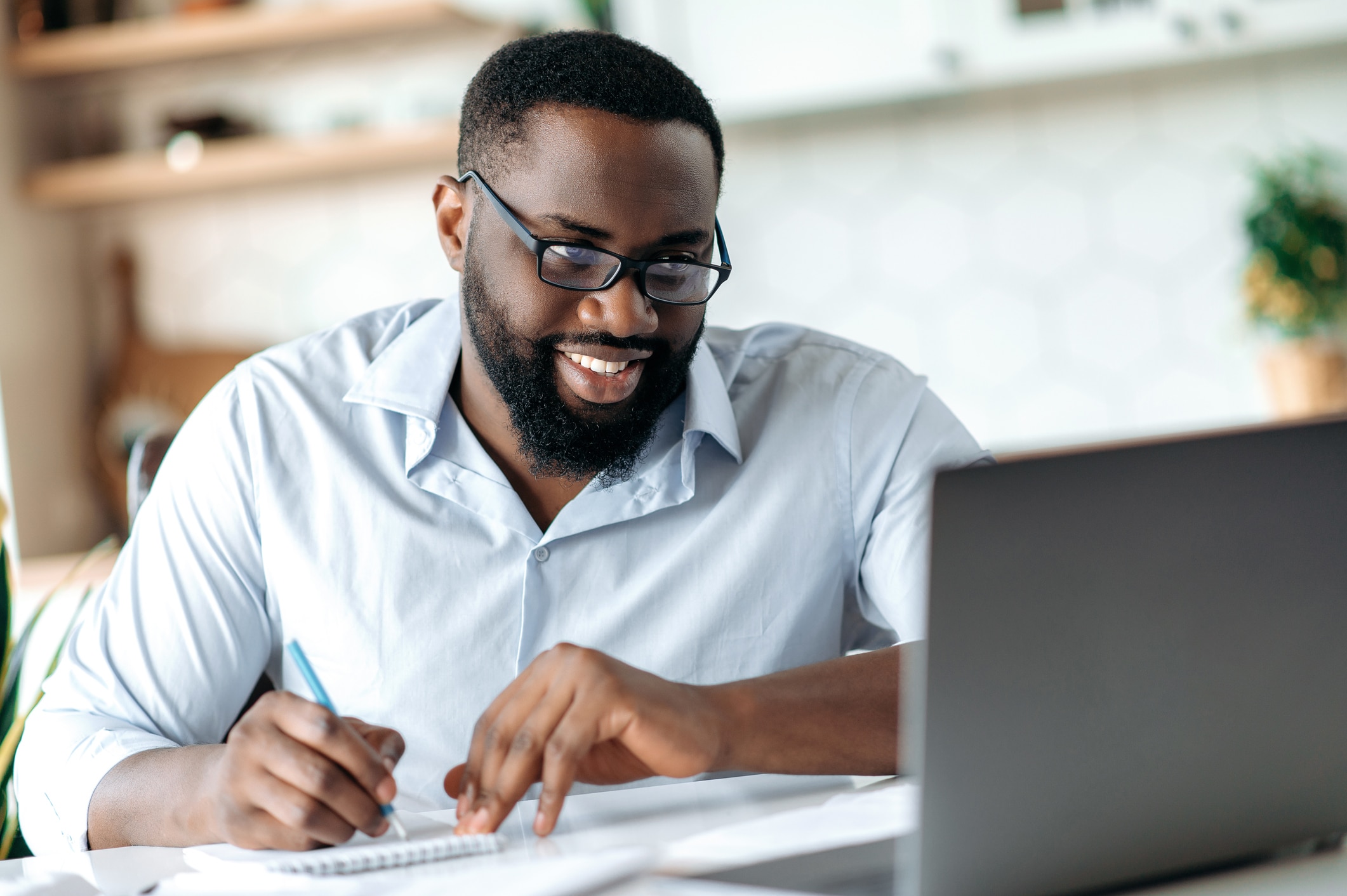 A male employee takes an online course and writes notes.