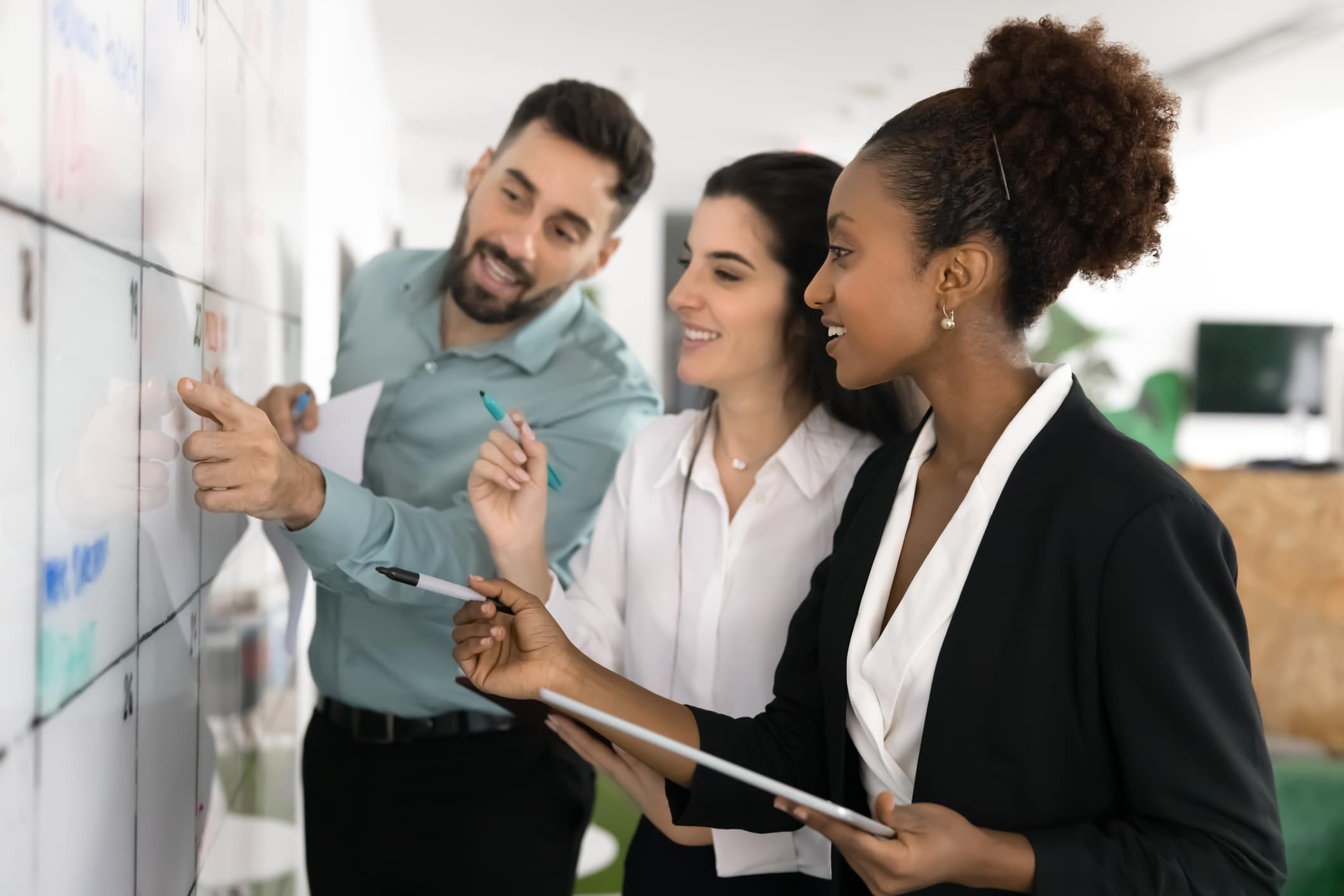 Three professionals collaborate at a whiteboard in an office, reviewing and discussing content together.
