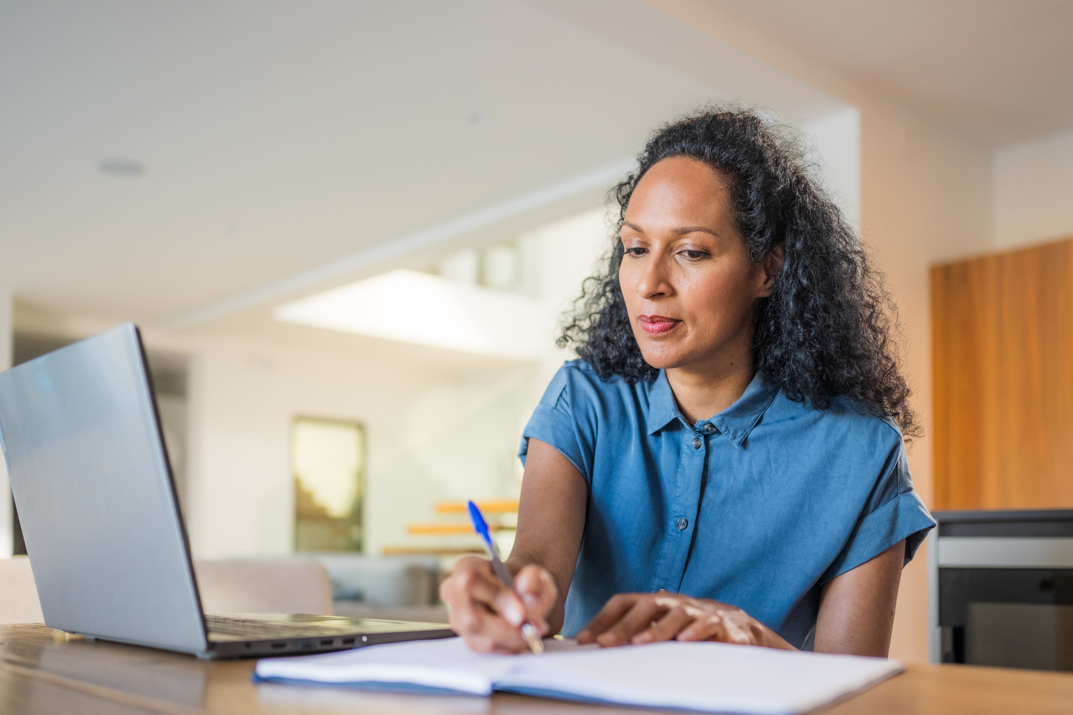 Woman looking at computer screen taking notes.